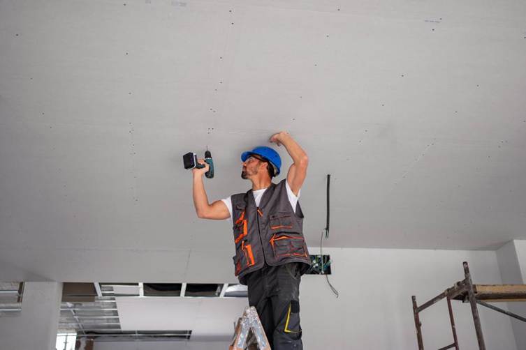 Homem trabalhando com parafusadeira para fixar as placas de drywall na estrutura metálica 